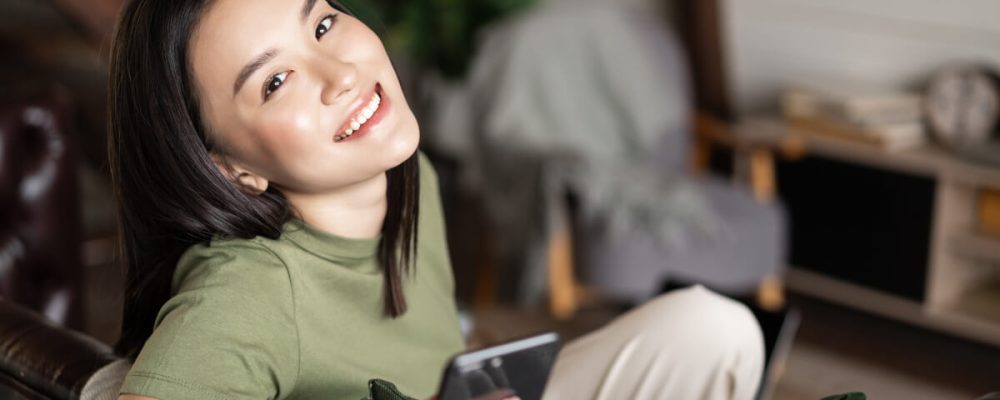 dreamy-smiling-asian-woman-using-mobile-phone-sit-2021-12-09-20-53-13-utc.jpg